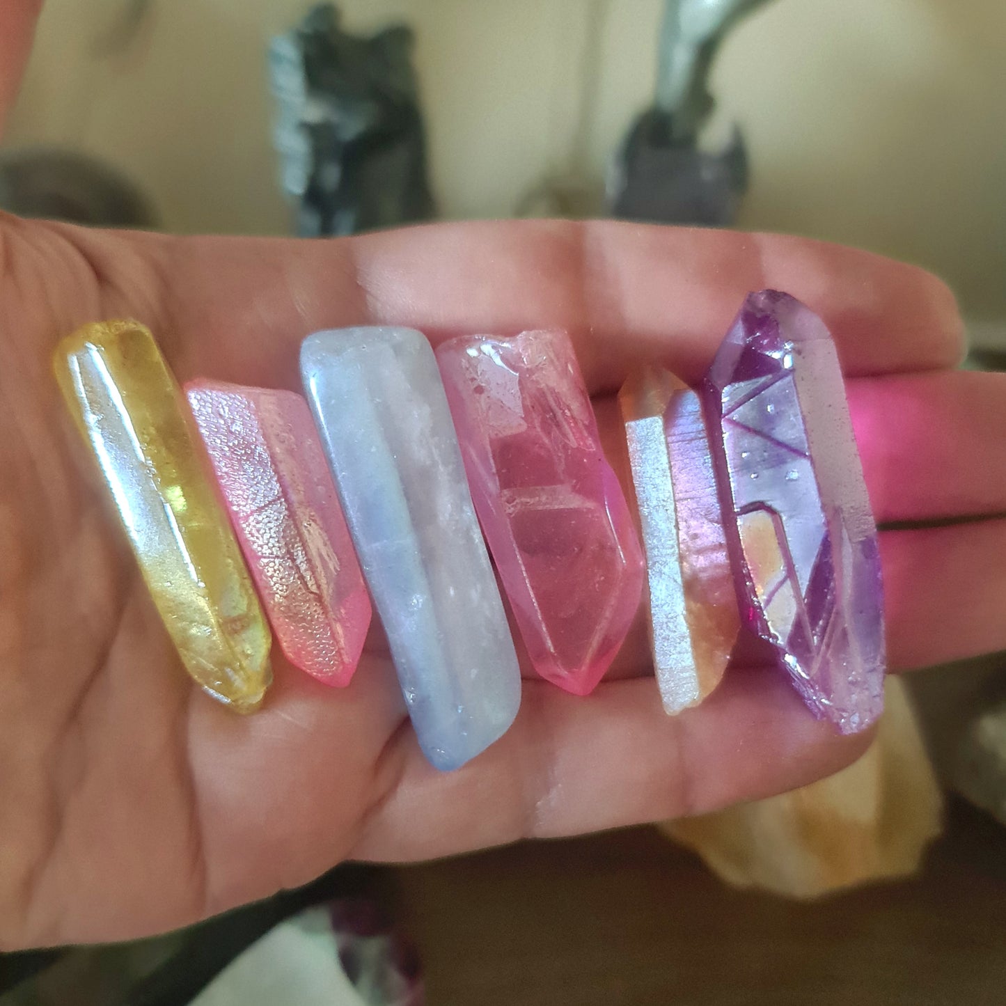 A collection of Aura Quartz crystals in various colors held in a person's hand.