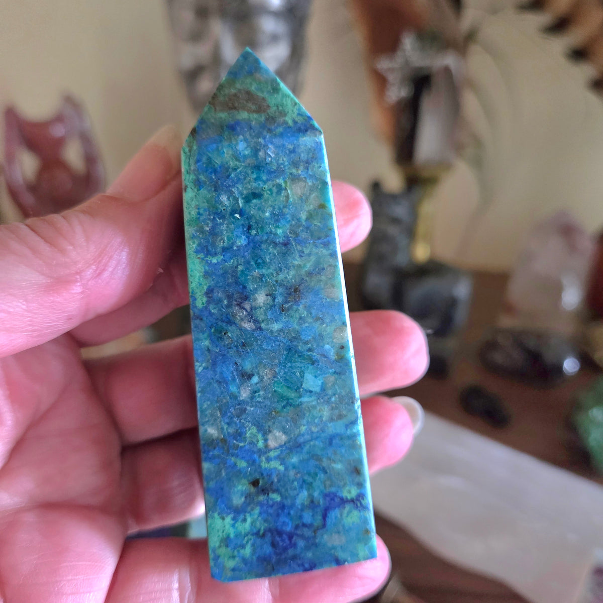 Hand holding a blue and green crystal with a blurred background