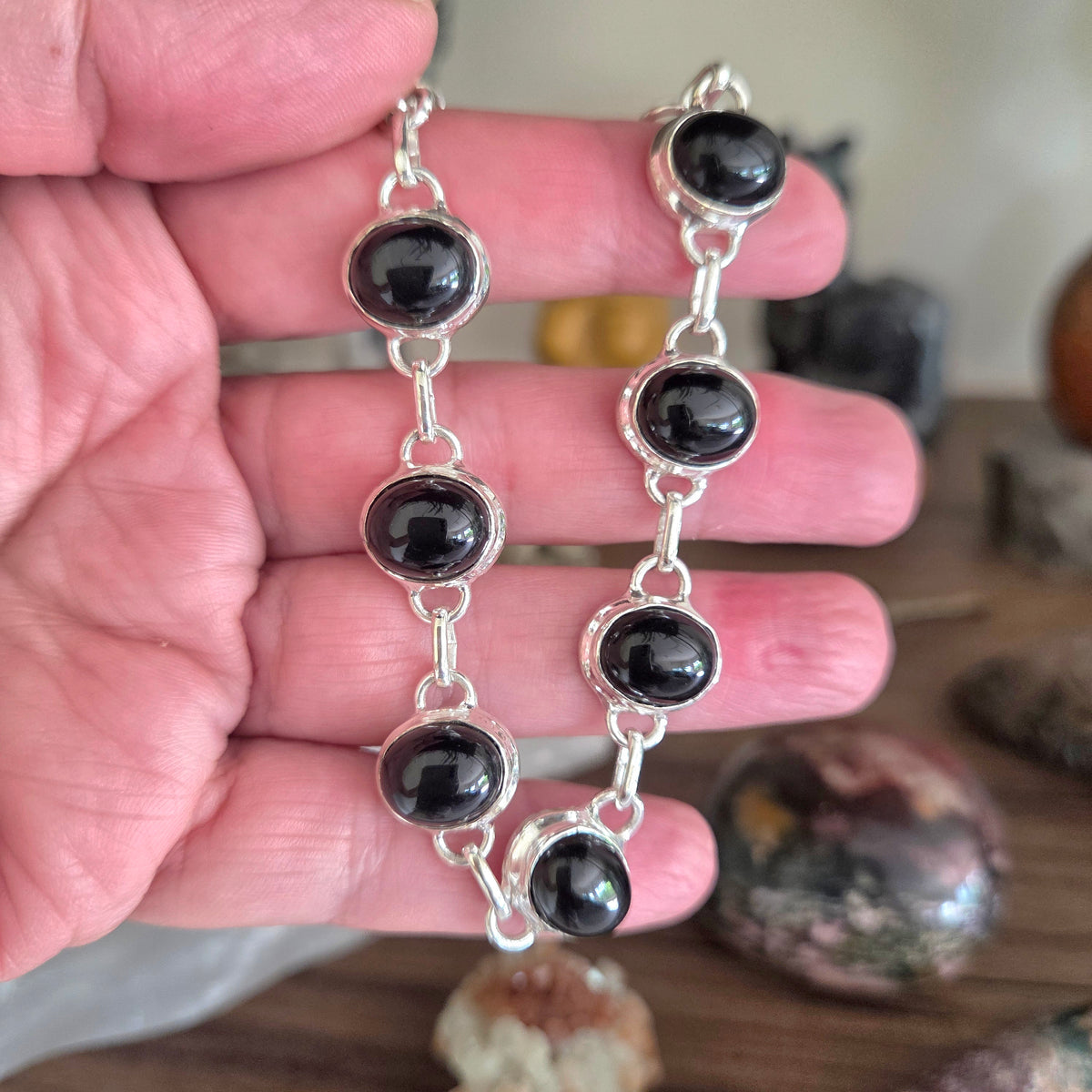 Silver bracelet with black beads held in a hand on a wooden surface.
