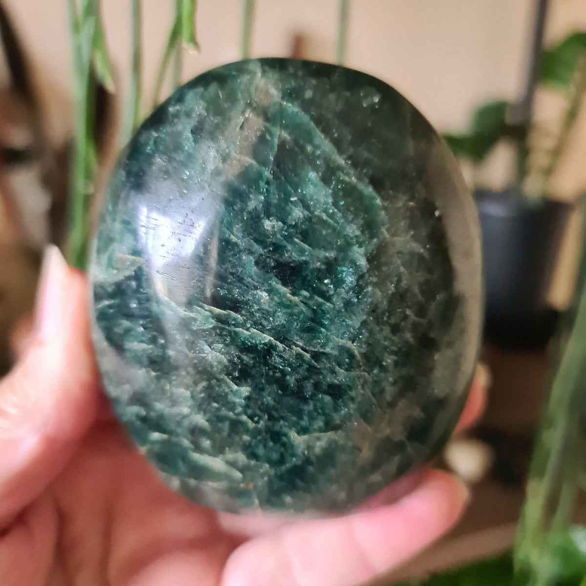 A polished green crystal stone with a natural blue-green coloring, held in a person's hand.