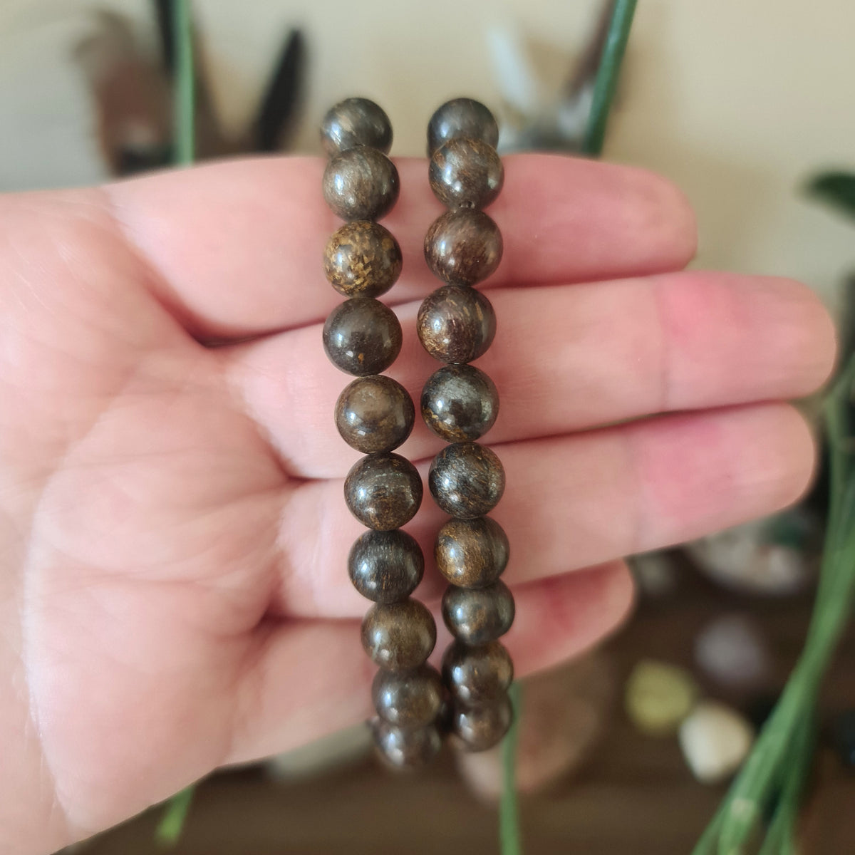 A hand holding a bronzite bead bracelet with a mix of brown and gray colors.