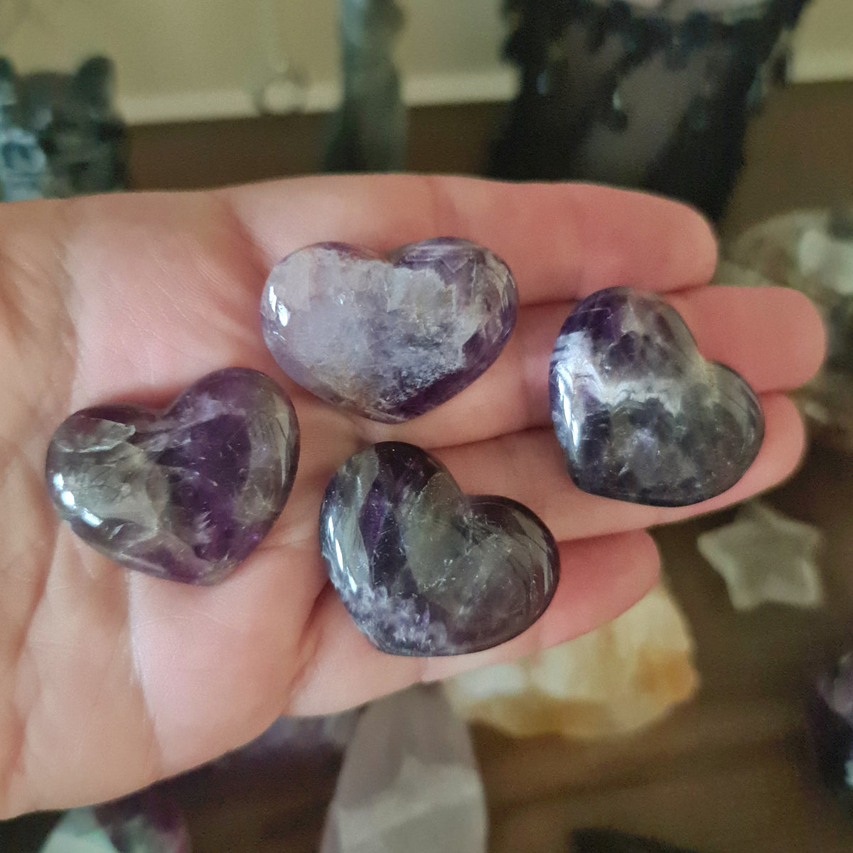 A hand holding a polished heart-shaped Chevron Amethyst crystal.