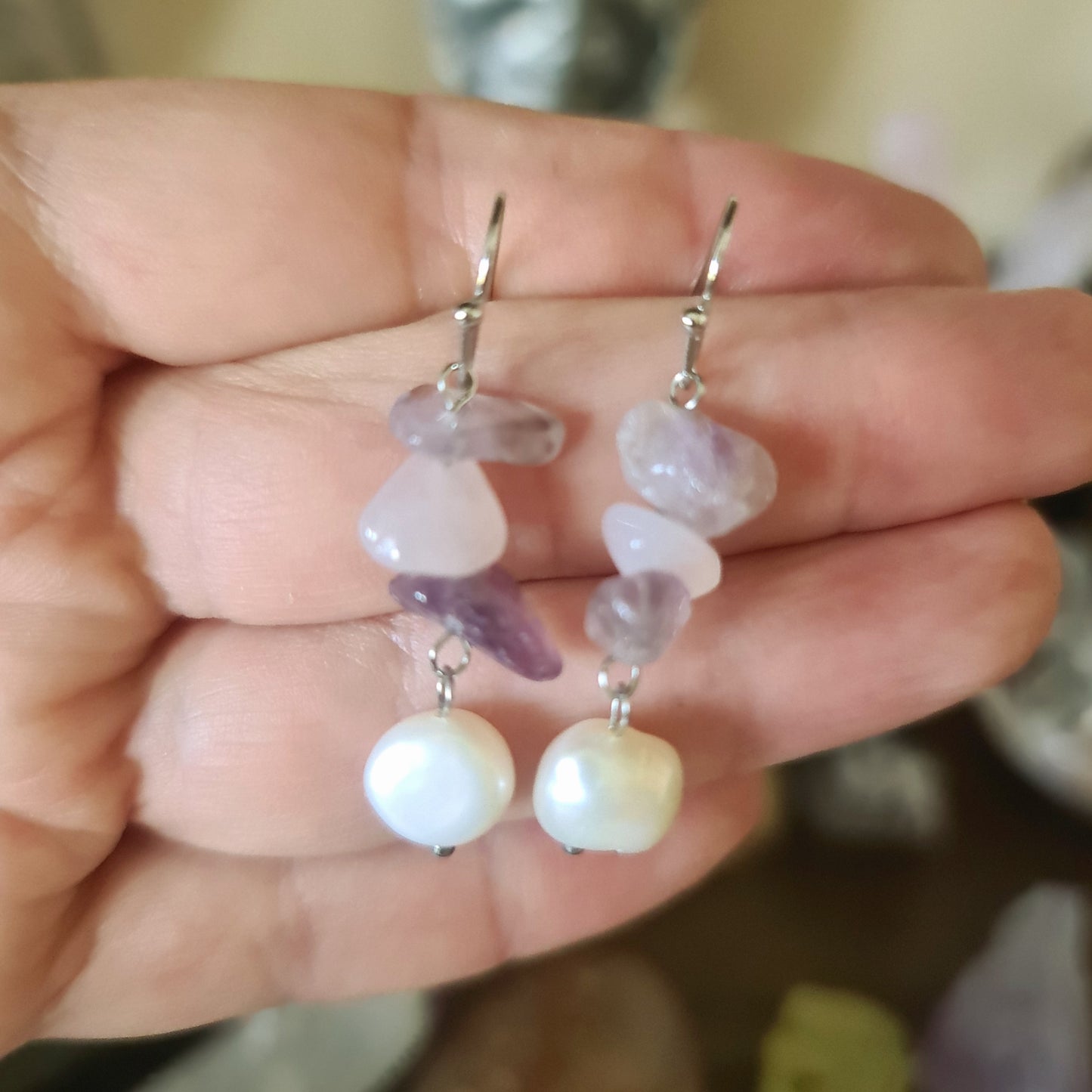 A hand holding a pair of pearl earrings with intricate designs, showcasing a mix of purple, clear, and white colors.