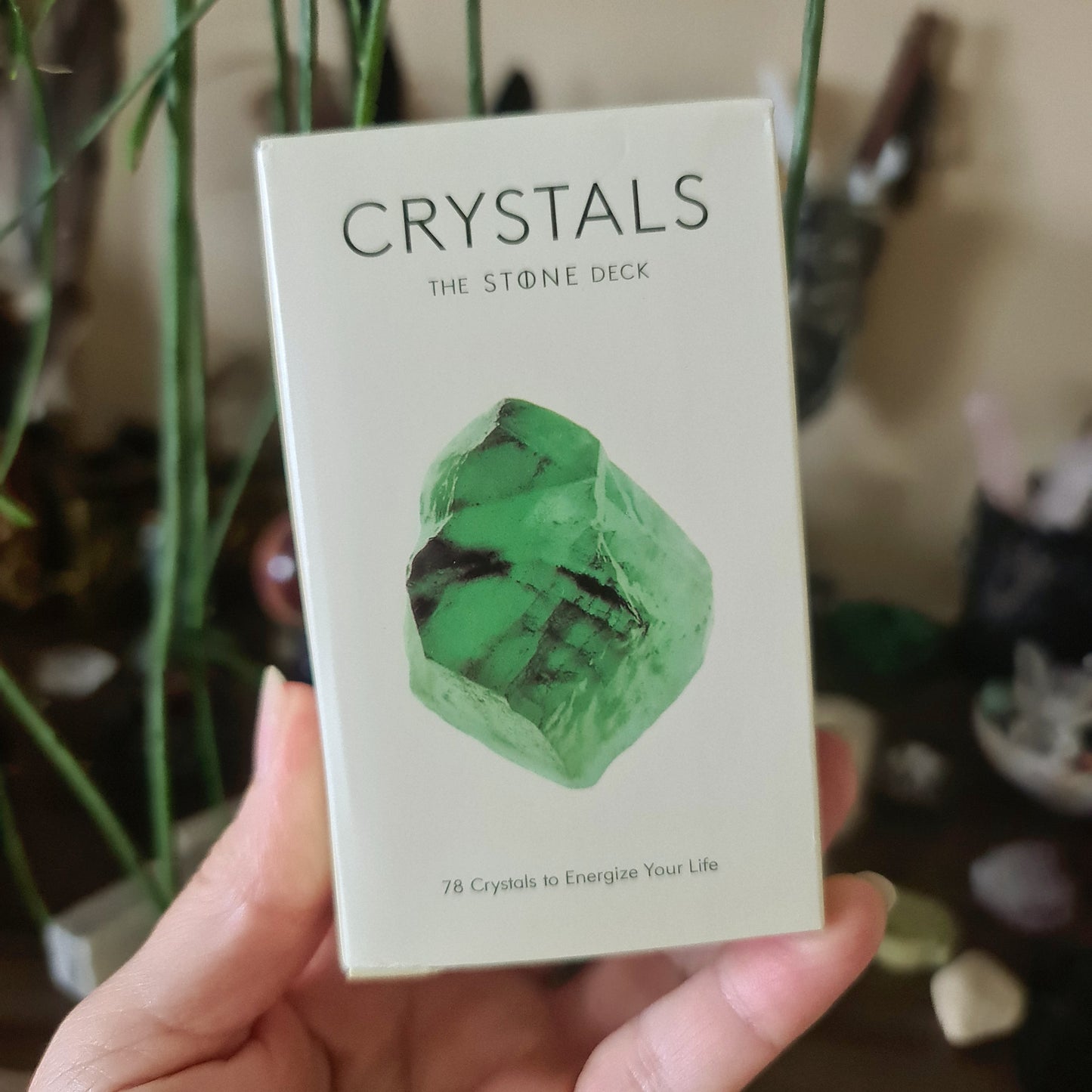 A hand holding a boxed deck of 'Crystals the Stone Deck' with a green crystal card visible on the top.