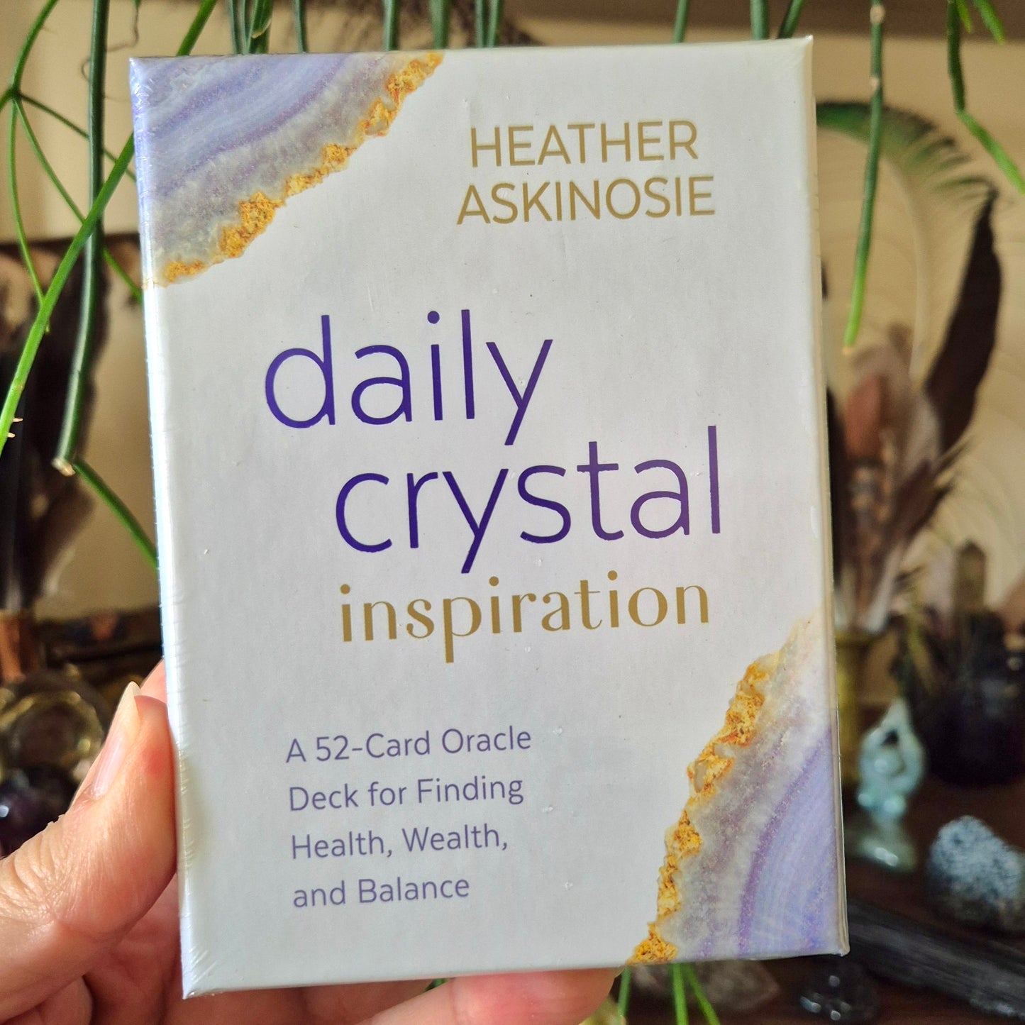A hand holding a pack of 'Daily Crystal Inspiration' cards with a blue and gold cover design.