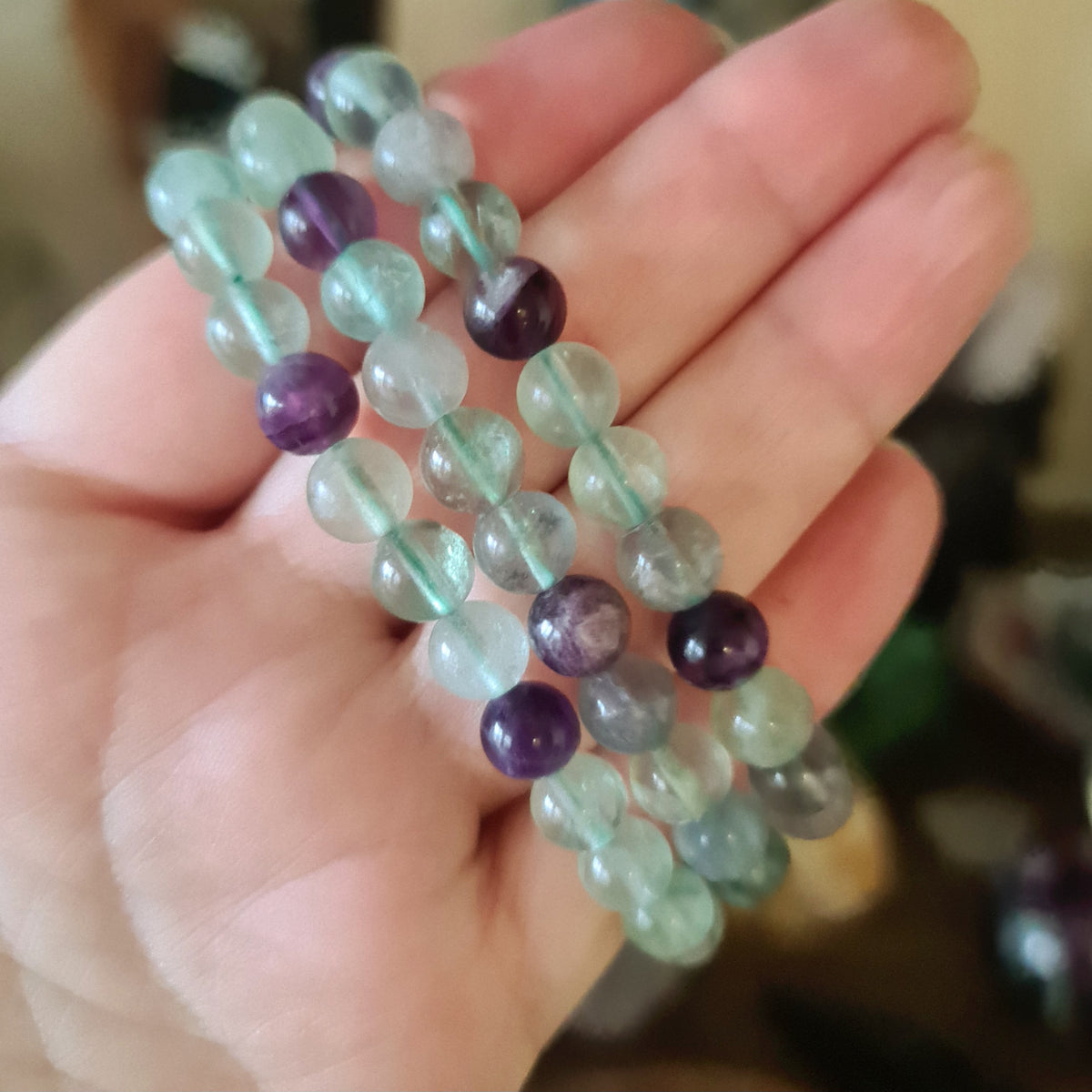 A hand holding a fluorite bracelet with a mix of purple, green, and clear colored beads.