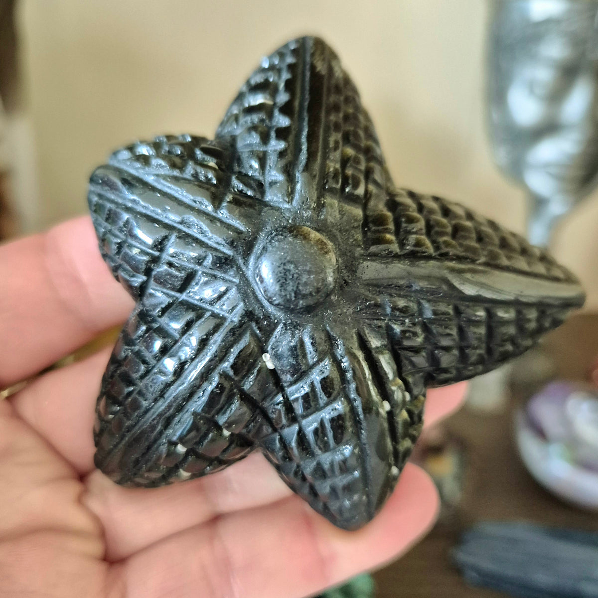 A small, dark gray obsidian starfish-shaped decoration being held in a person's hand.