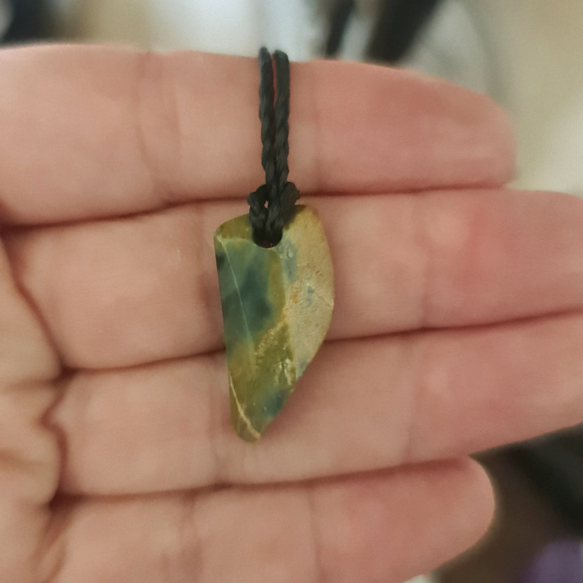 A person holding a Guatemalan Jadeite necklace with an adjustable leather strap.