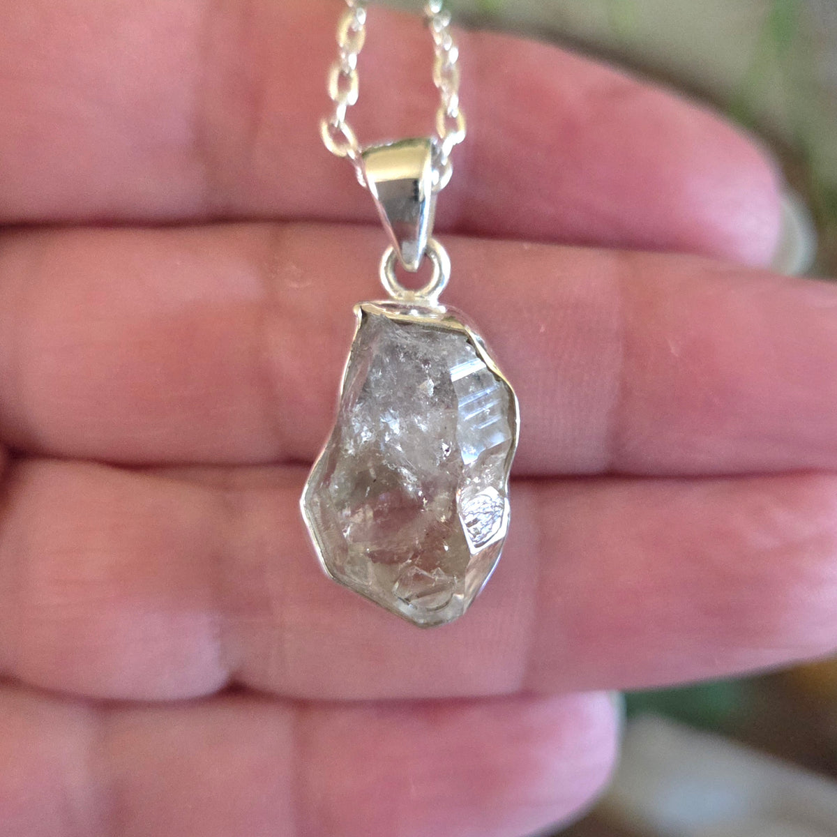 Raw diamond pendant on a silver chain held in a hand.