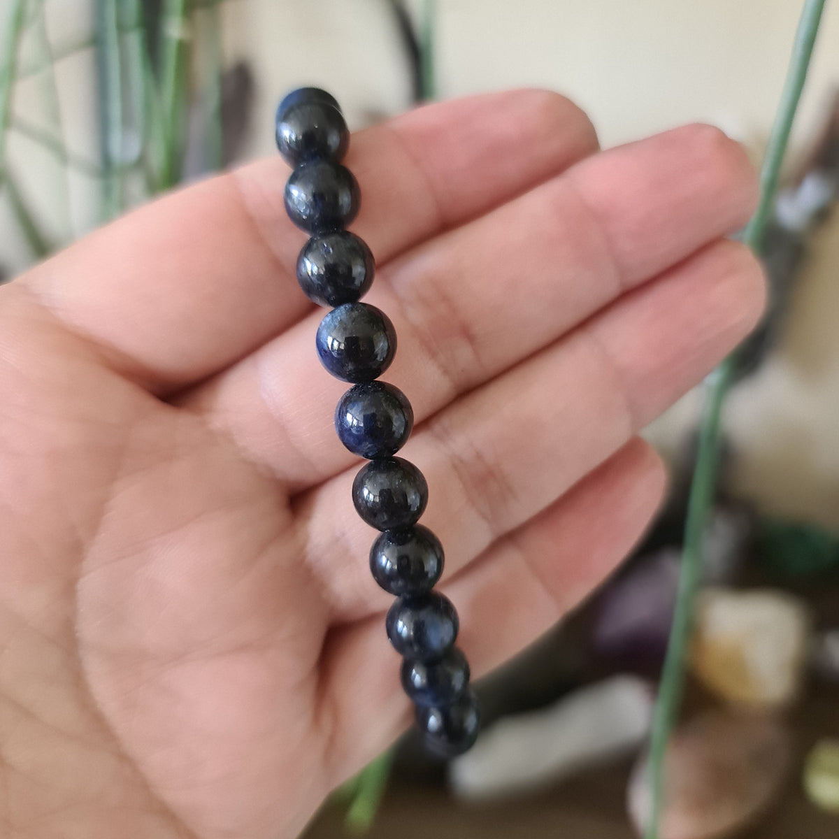 A hand holding a series of blue kyanite beads, with a focus on the last bead in the string.