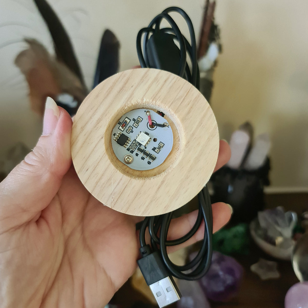 A person holding a round LED light base with a timber (wooden) base and an attached USB cable.