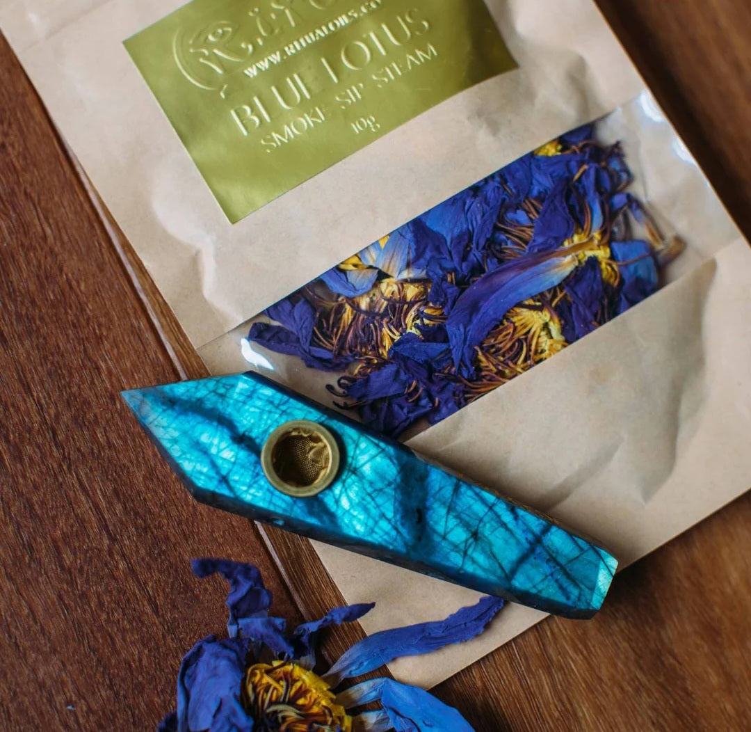 A labradorite stone pipe with blue tinges, alongside a packet labeled 'Blue Lotus', with a pipe cleaner and a black satin bag.