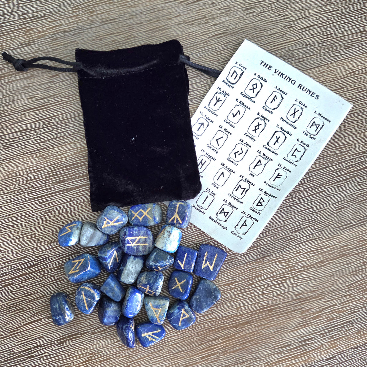 Set of blue rune stones with a black drawstring bag and rune chart on a wooden surface