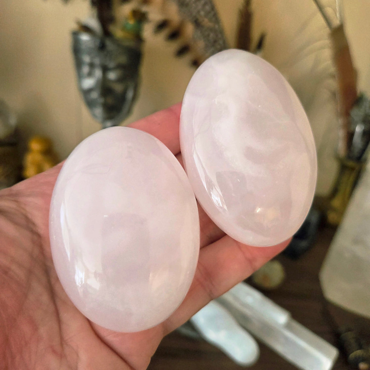 Two palm-sized Mangano Calcite stones held in a person's hand, displaying a translucent pink color.