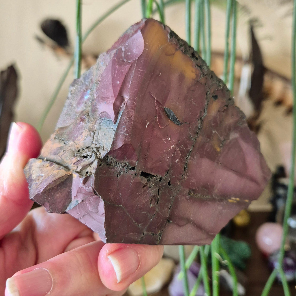 A polished Mookaite Jasper Chunk held in a person's hand, with a reddish-purple color and natural patterns.