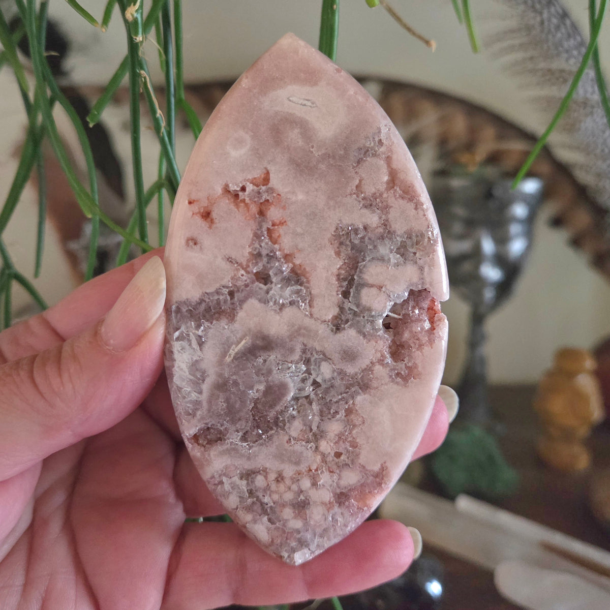 Hand holding a polished stone with intricate patterns, blurred indoor background