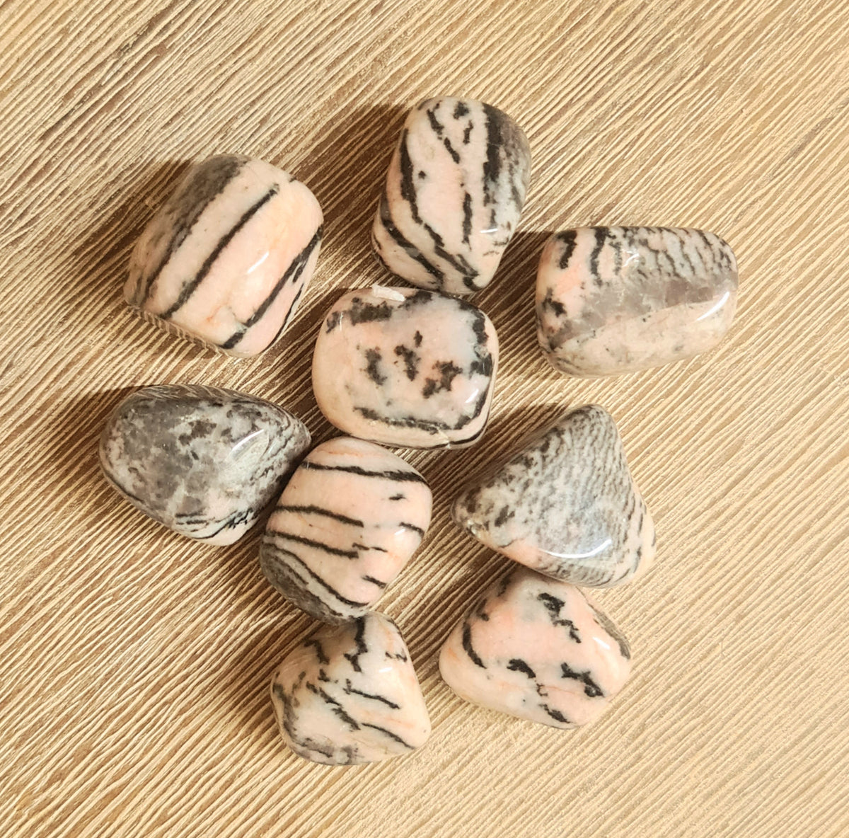 A collection of pink zebra jasper tumbles with black stripes on a wooden surface.