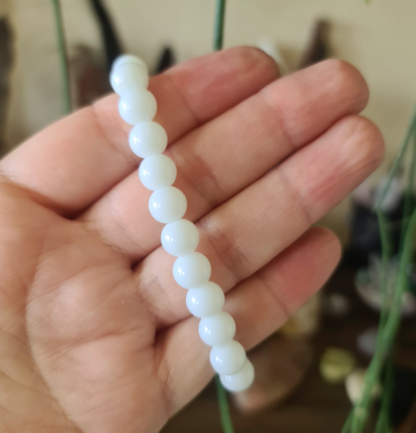 A hand holding a porcelanite bracelet with smooth, rounded beads.