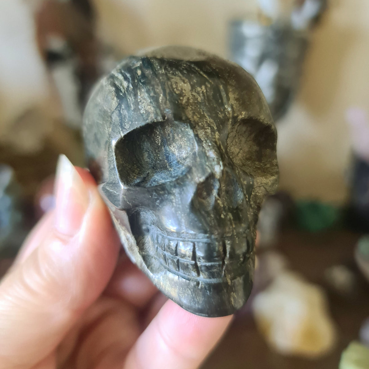 A small pyrite skull figure held in a person's hand, with a textured, rugged appearance in a metallic color.