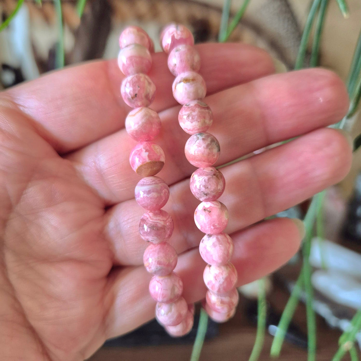 A person holding a rhodochrosite bracelet with pink and brownish polished beads.