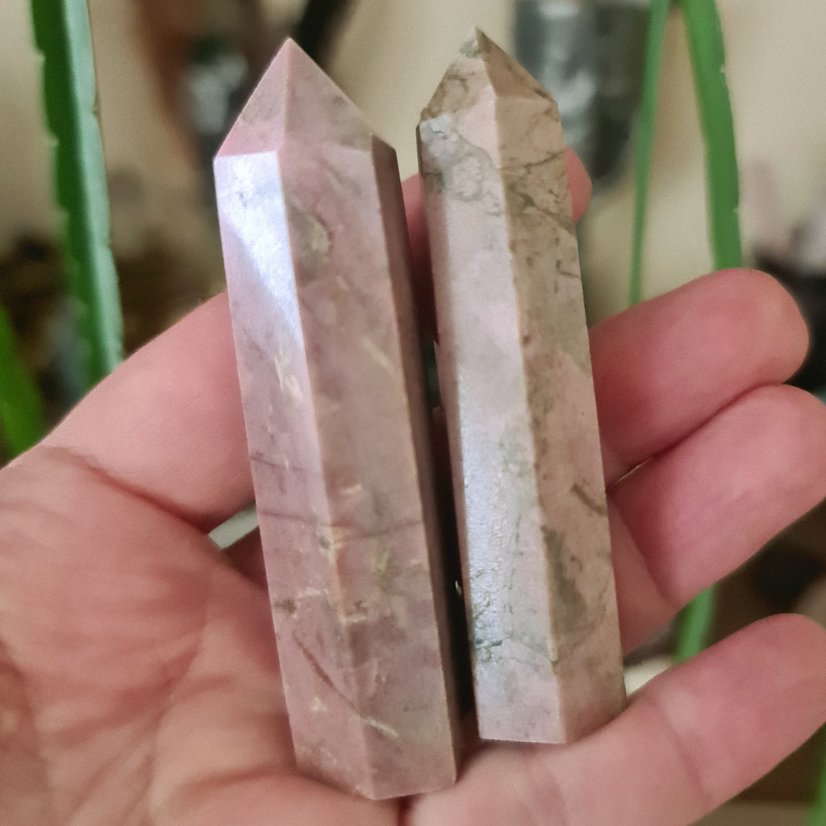 Two polished Rhodonite crystal points with a pink and brown color scheme, held in a person's hand.