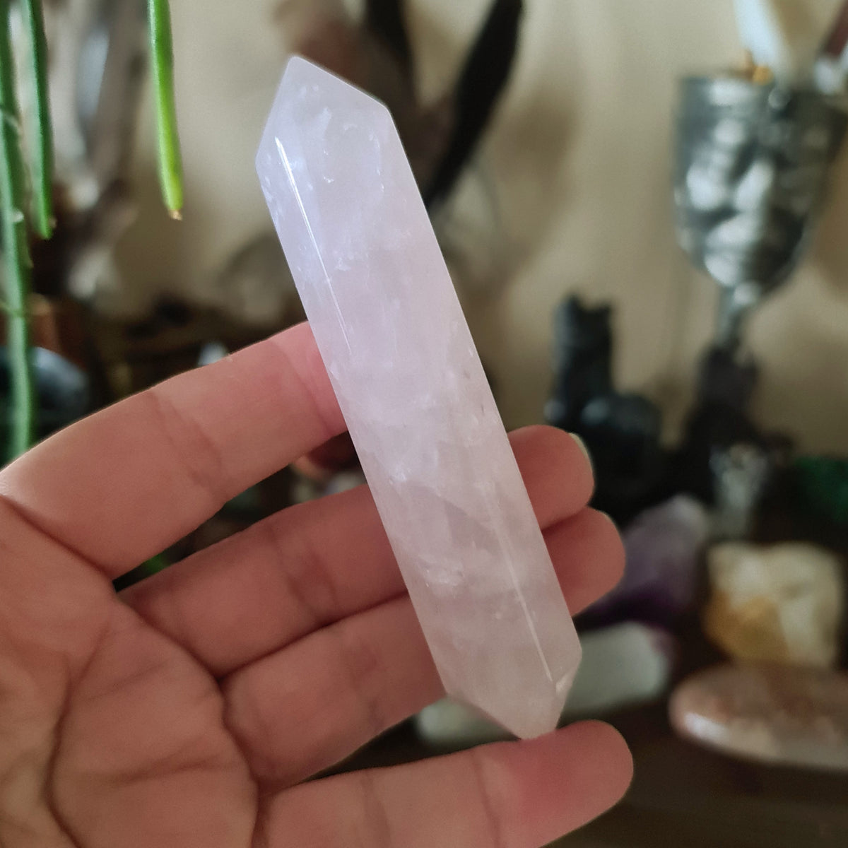 A hand holding a polished, pink-colored Rose Quartz crystal with a double point.