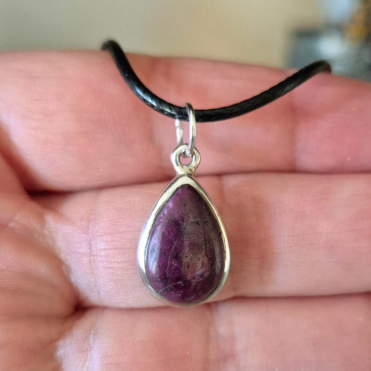 A sterling silver ruby pendant held in a person's hand, with a black chain attached to it.