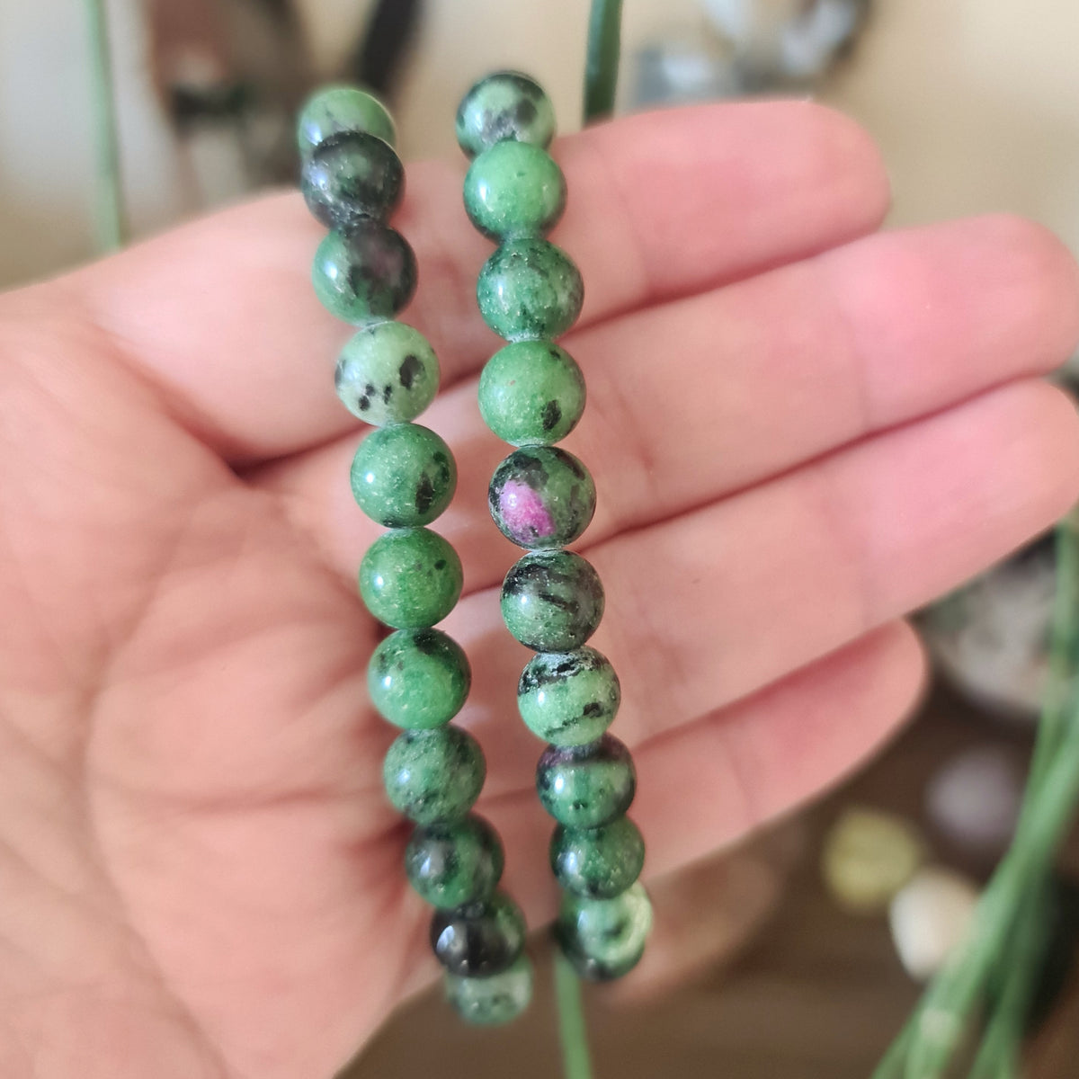 A hand holding a bracelet with green and black stones, with a focus on the beads and the bracelet's closure.