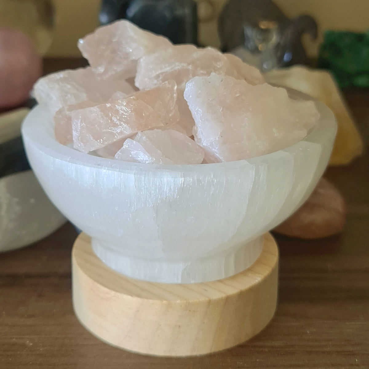 A white selenite bowl lamp with rose quartz crystals on a wooden base, featuring an LED light.
