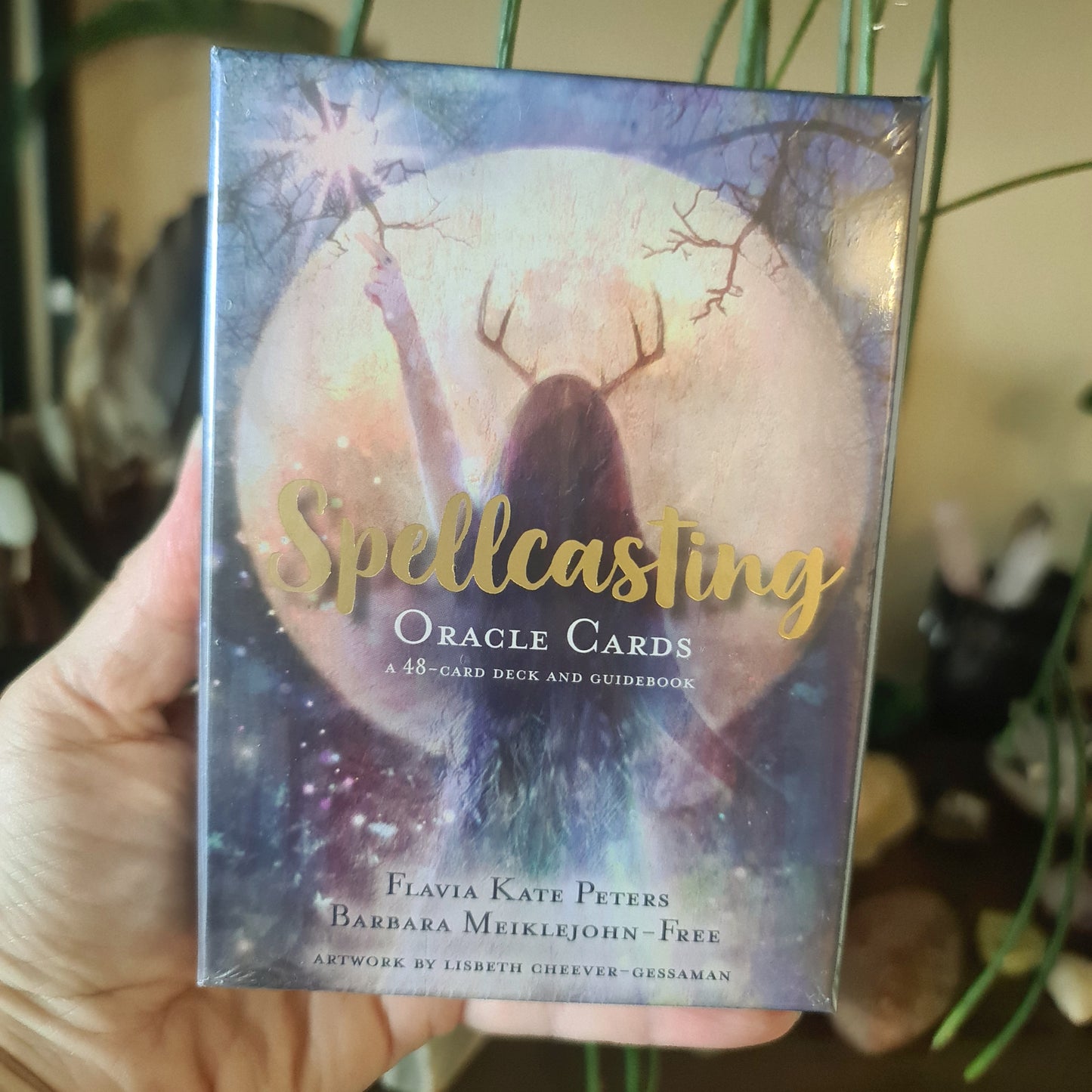 A hand holding a box of 'Spellcasting Oracle Cards' with a visual of a woman in a moonlit forest setting the tone for the mystical and magical theme of the product.