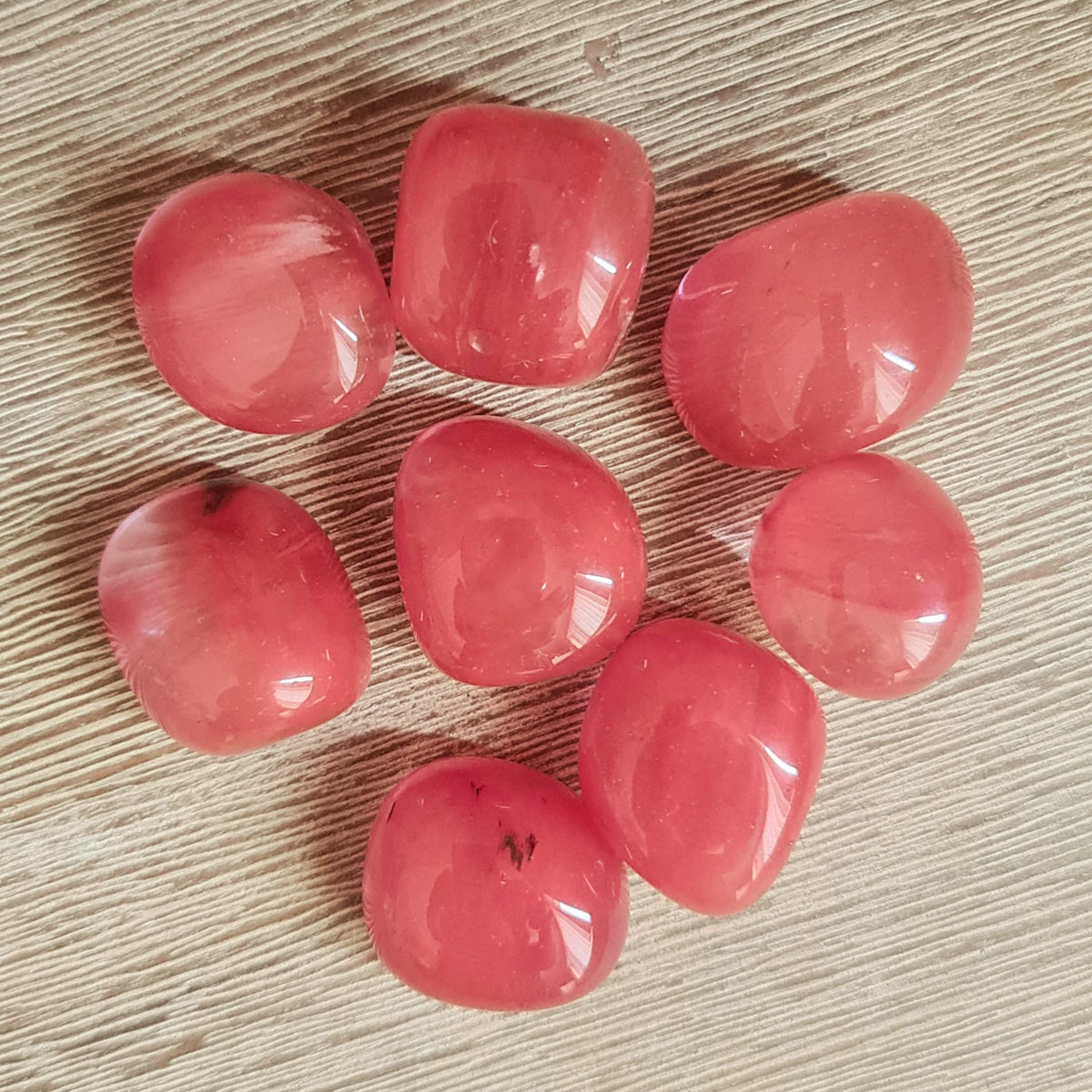 A collection of Strawberry Obsidian stones with a red/pink color, arranged on a wooden surface.