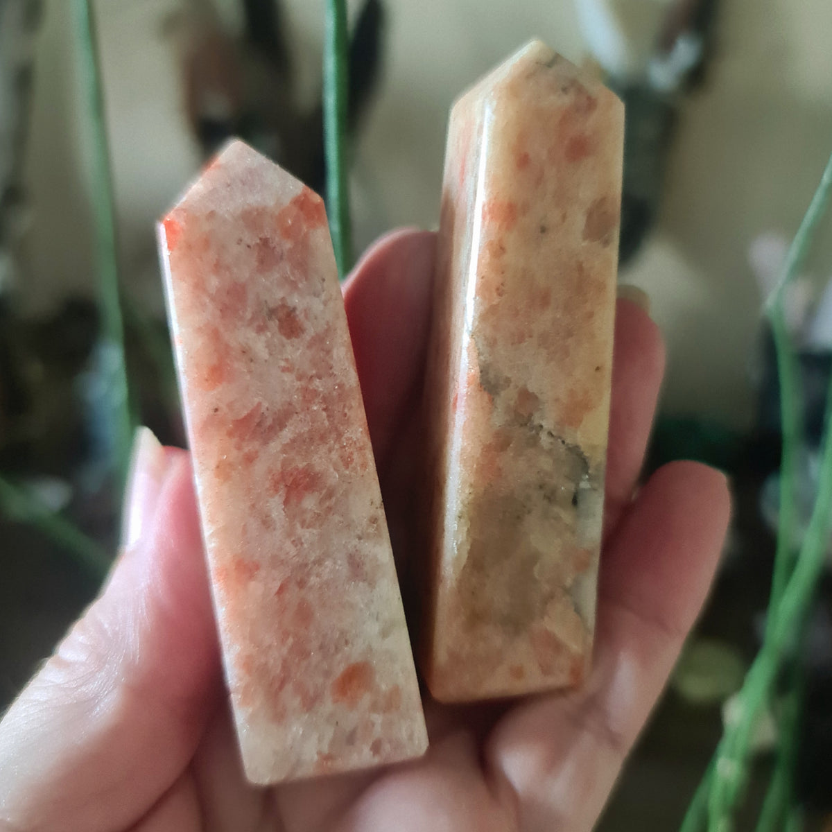 A polished sunstone with a reddish-orange coloring, held in a person's hand.