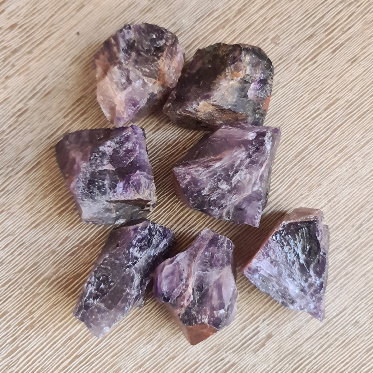 A collection of raw, unpolished Super Seven chunks laid out on a beige surface.