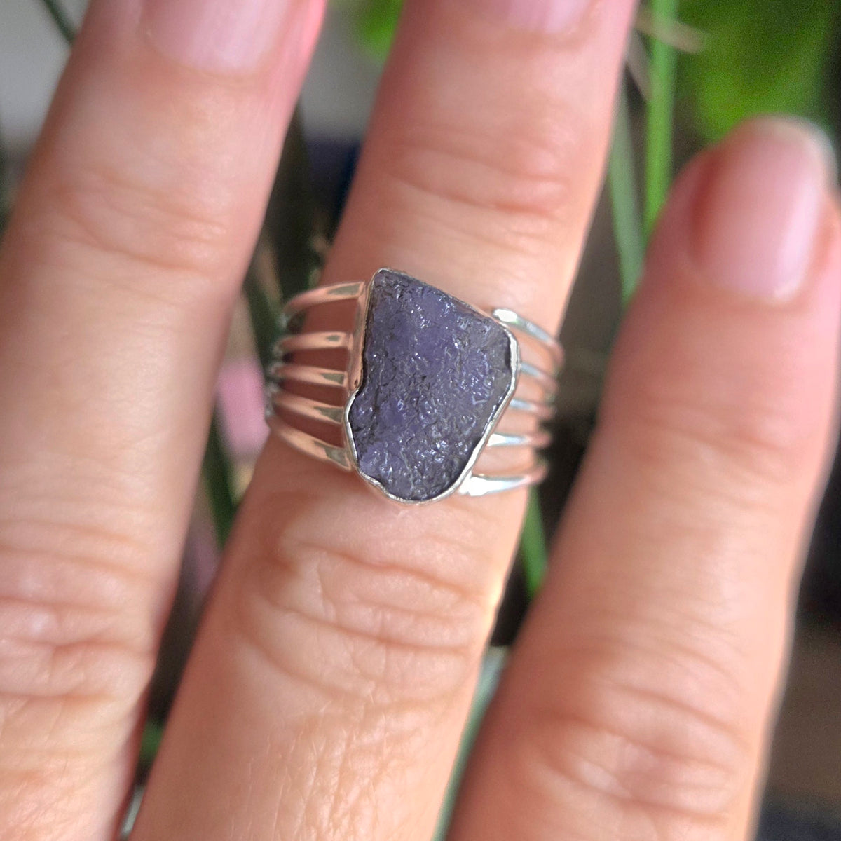 Silver ring with a purple stone on a finger against a blurred natural background