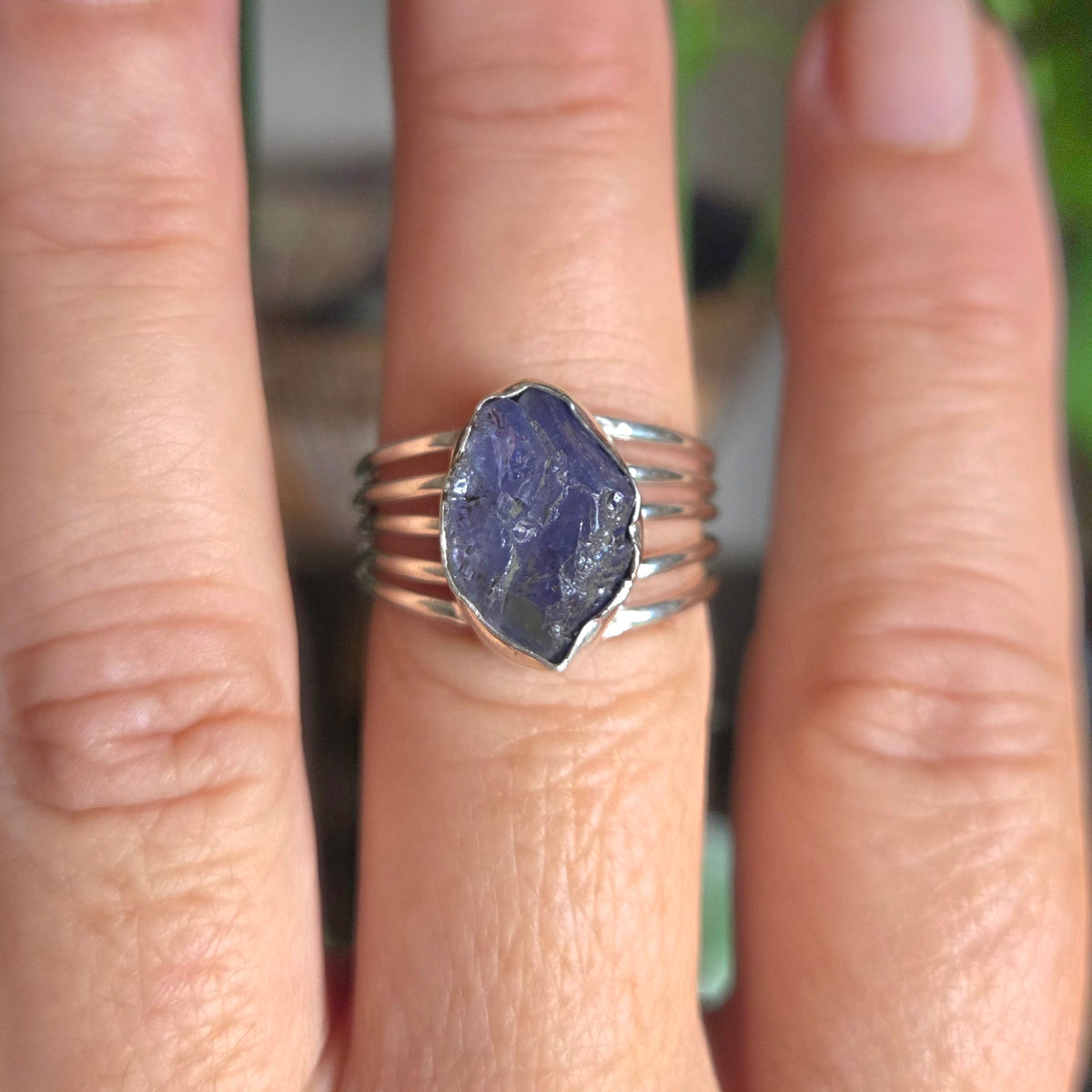 Close-up of a hand wearing a ring with a purple stone on a blurred natural background