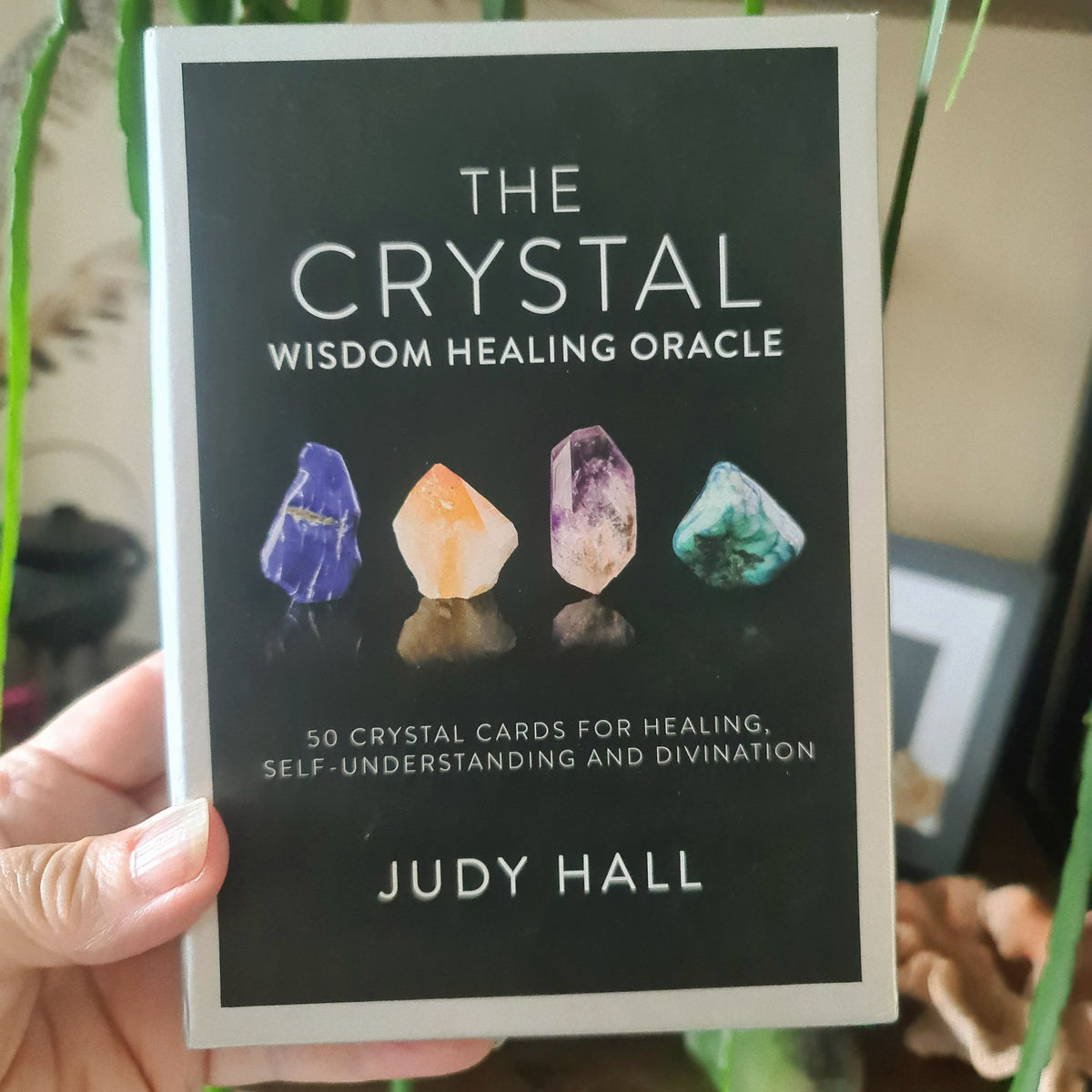 A book titled 'The Crystal Wisdom Healing Oracle' by Judy Hall, featuring a black cover with illustrations of various colorful crystals.