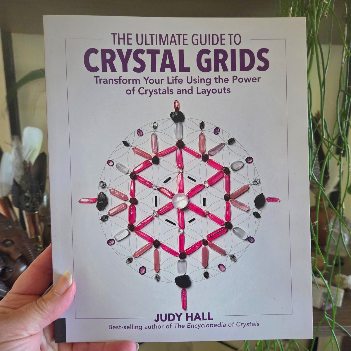 Book titled 'The Ultimate Guide to Crystal Grids' held by a hand with a blurred background