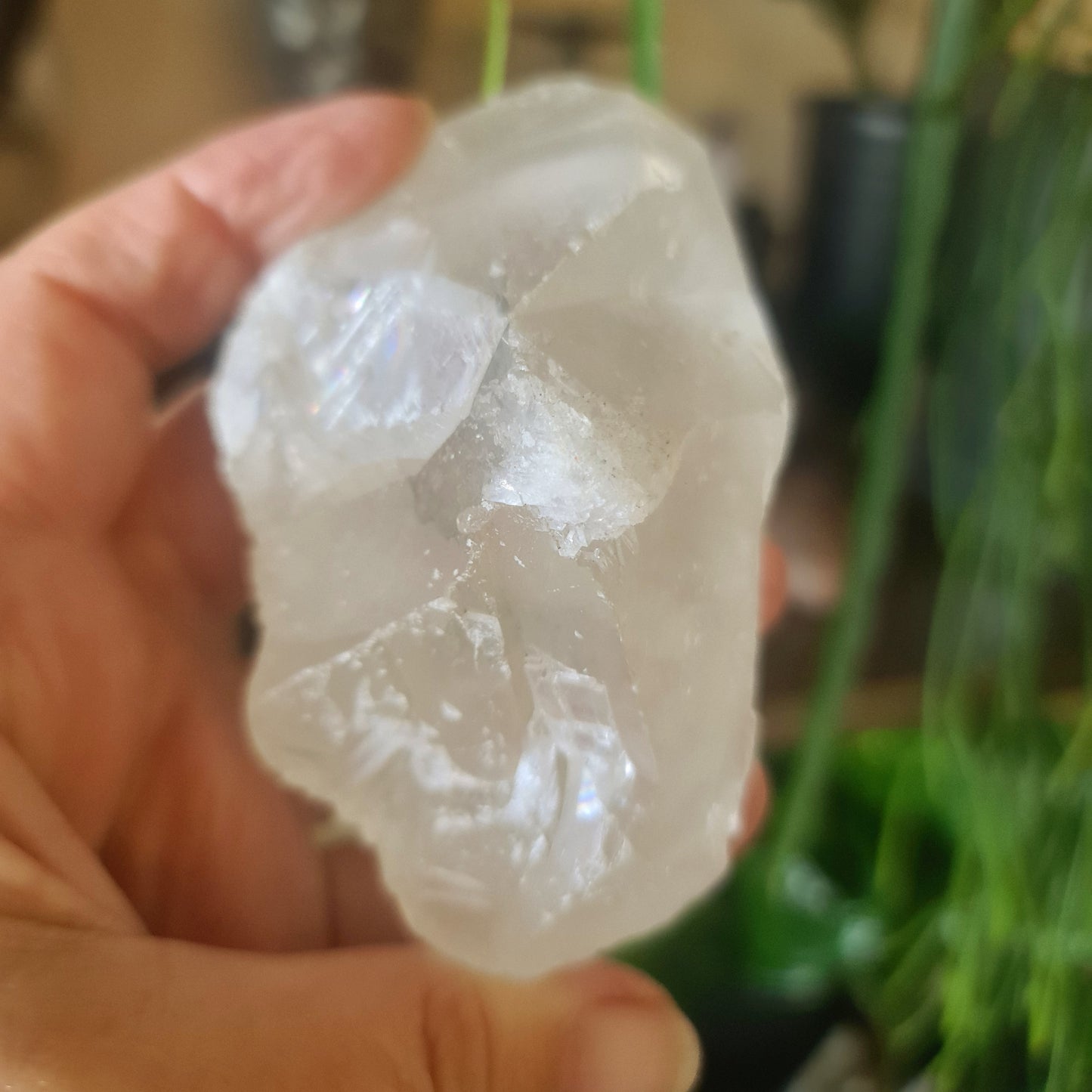 A hand holding a clear, irregularly shaped zeolite chunk, with a blurred background suggesting a indoor setting
