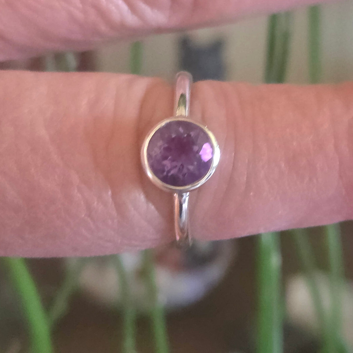Silver ring with a purple gemstone on a finger against a blurred green background