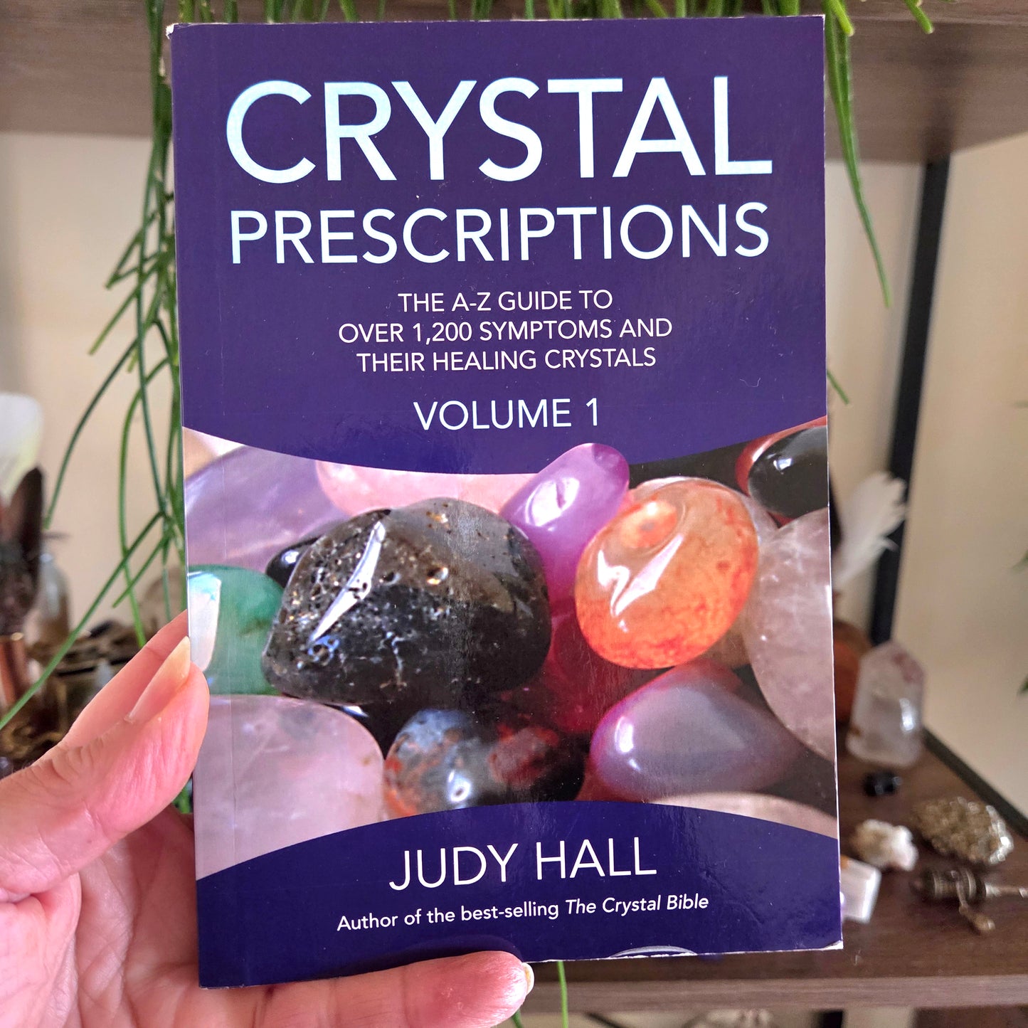Book titled 'Crystal Prescriptions' by Judy Hall held in a hand with a blurred background