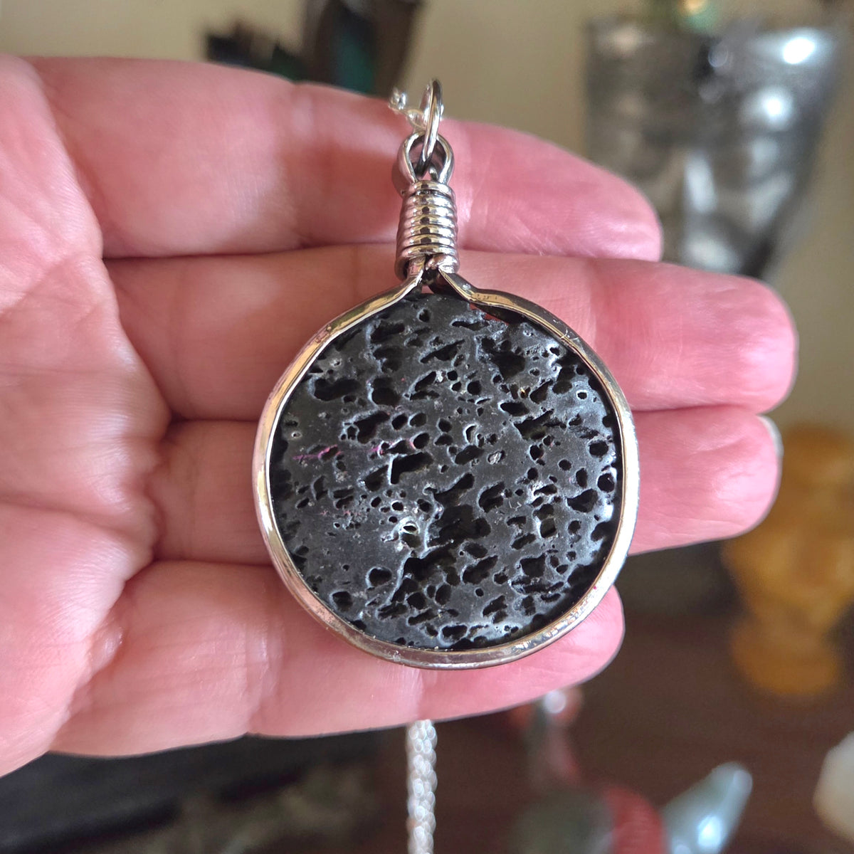 Hand holding a textured silver pendant with a blurred background