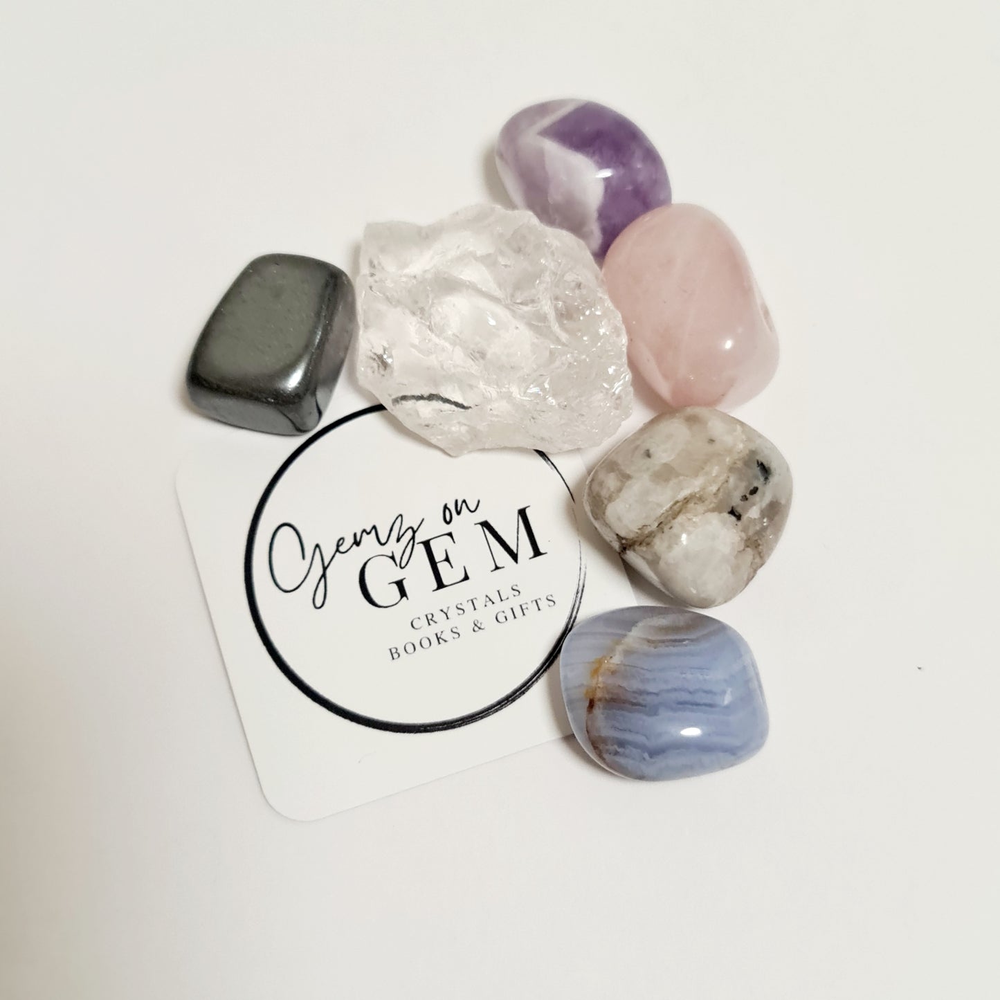 An assortment of polished gemstones including rose quartz, amethyst, blue lace agate, moonstone, and hematite, displayed on a card with 'Gemz on Gem' branding.