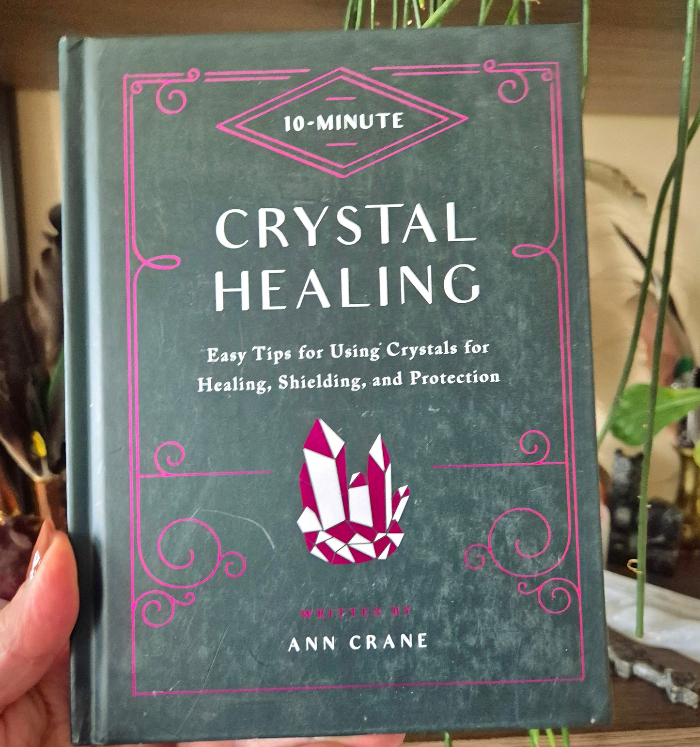 A book titled '10-Minute Crystal Healing' by Ann Crane, featuring a green cover with a pink and purple design and the author's name.