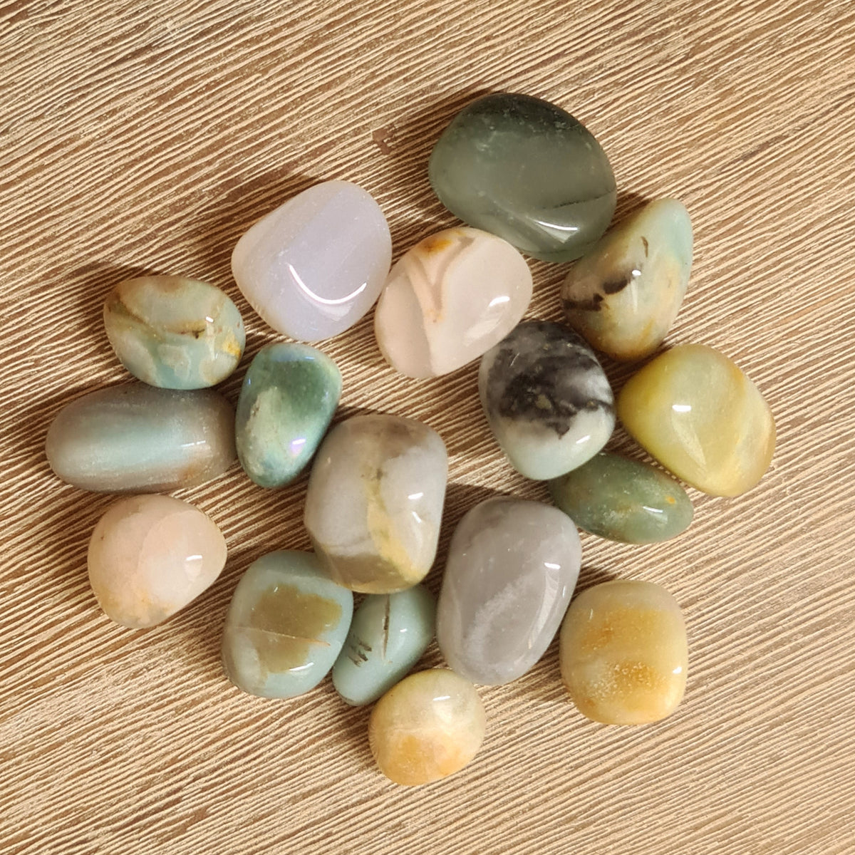 A collection of African Bloodstone tumble stones displayed on a wooden surface.