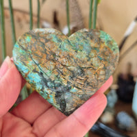 A heart-shaped piece of turquoise stone with a web-like pattern, held in a hand.