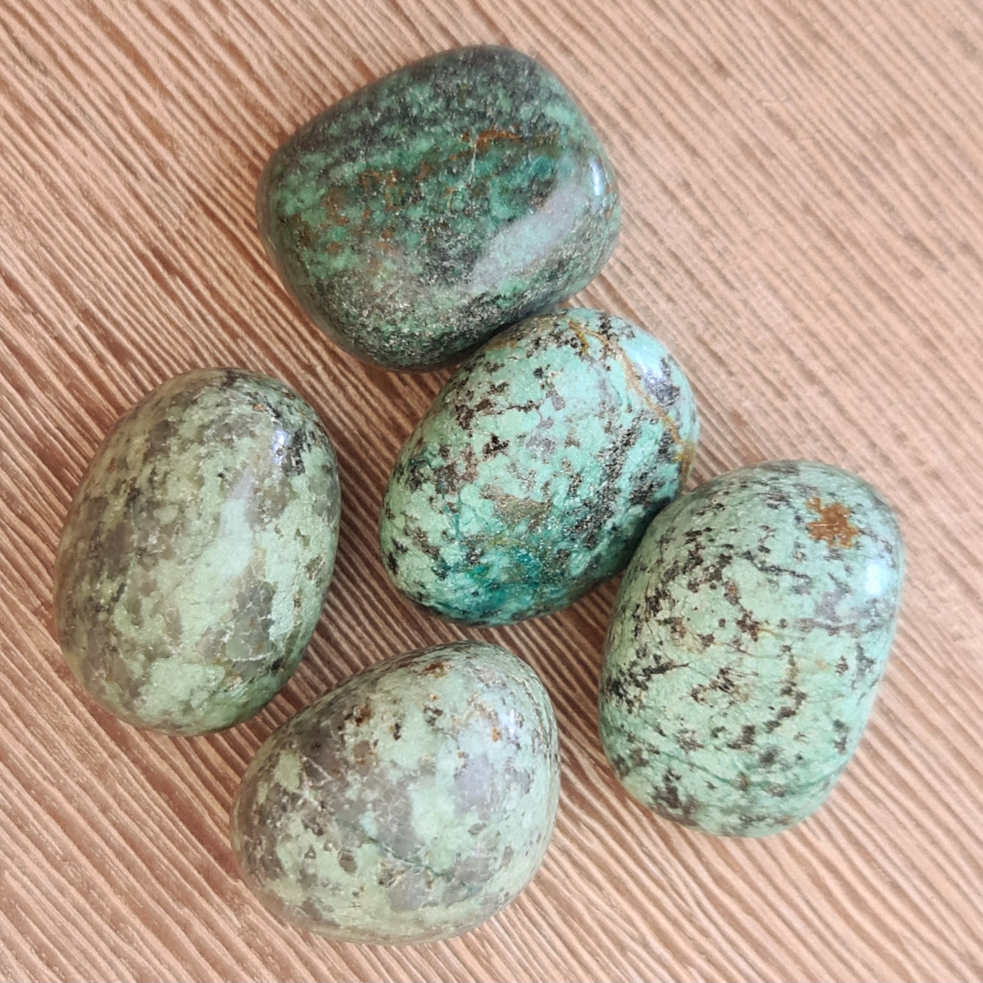A collection of polished African turquoise tumble stones displayed on a textured background.