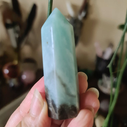 A polished amazonite crystal point being held in a person's hand, with a blurred background suggesting it is the main subject of the photo.