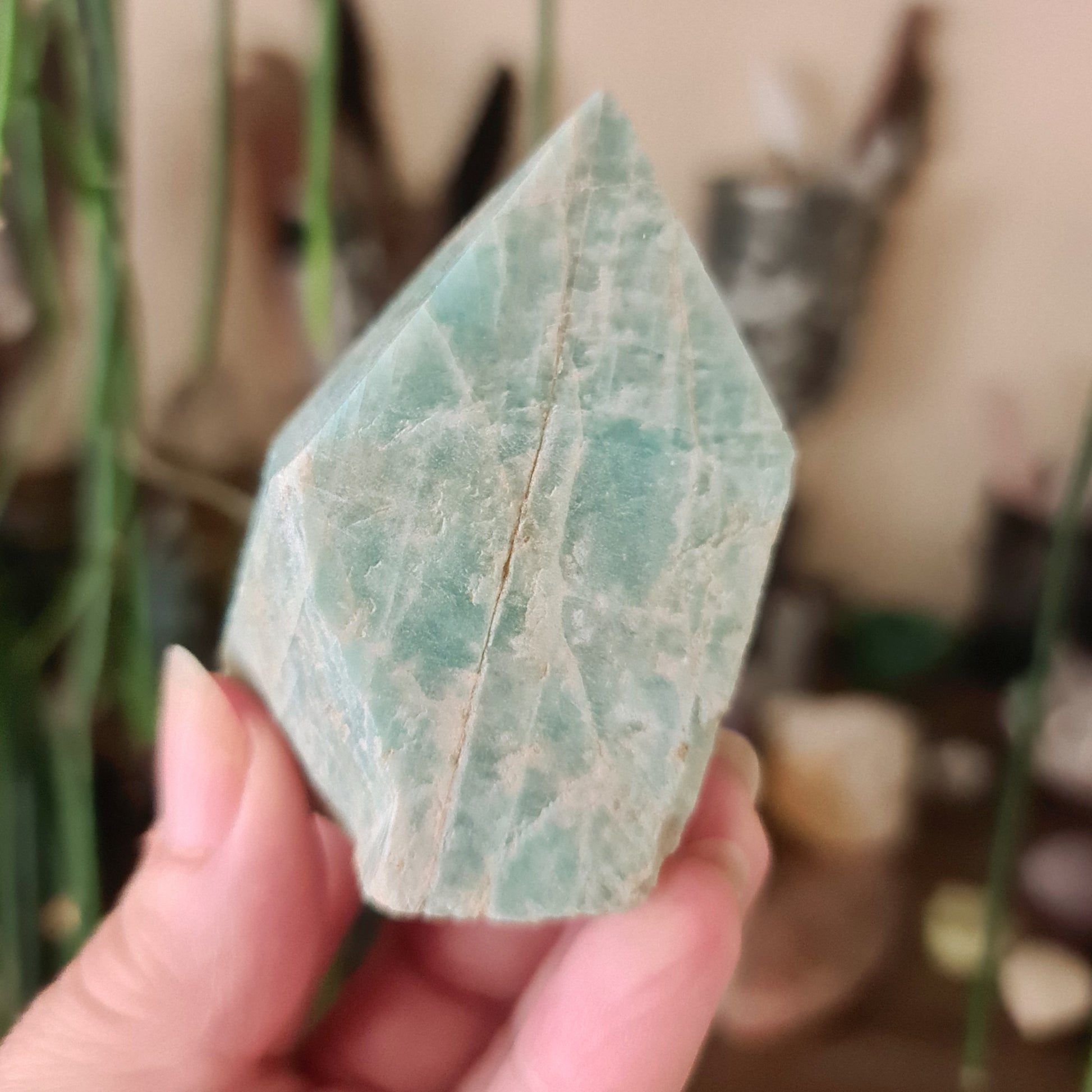 A polished point of amazonite green crystal held in a person's hand.