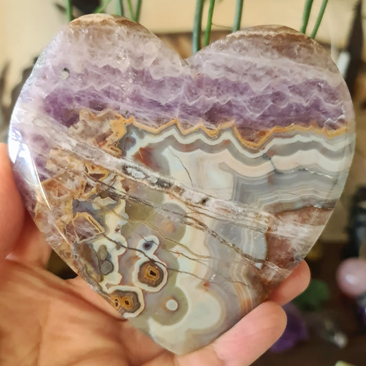 A heart-shaped Amethyst Agate slab held in a person's hand, displaying bands of purple and white with patterns.