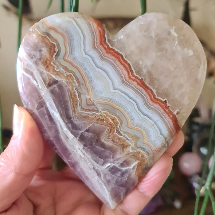 A heart-shaped Amethyst Agate slab held in a person's hand, displaying layered patterns of pink, white, and gray.